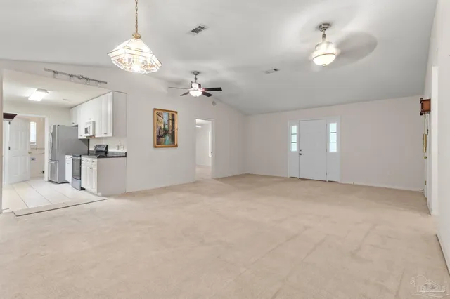 a view of an empty room with a chandelier fan and kitchen view