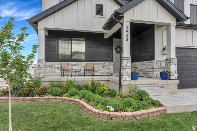 Contemporary exterior featuring white board and batten siding, dark horizontal siding, a stone facade, a covered front porch, and a landscaped front yard with a retaining wall
