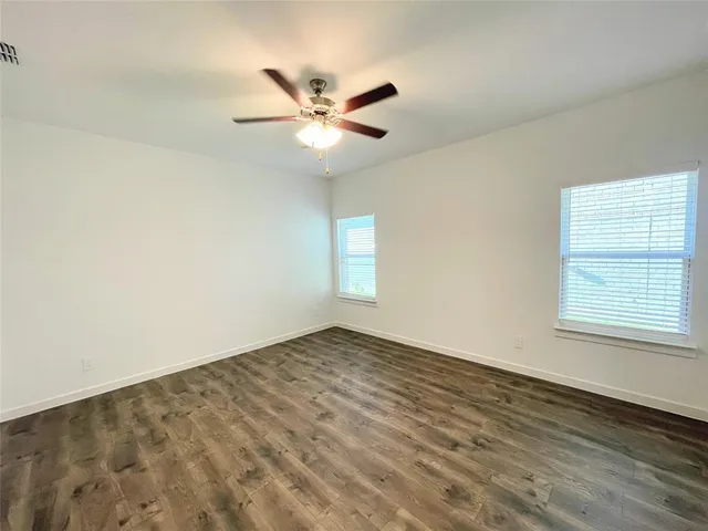 an empty room with wooden floor fan and windows