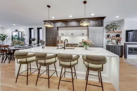 a kitchen with stainless steel appliances kitchen island granite countertop a dining table chairs and a refrigerator