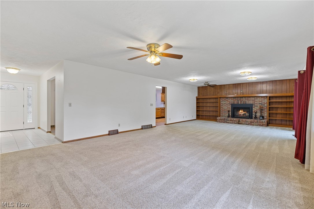 16295 Sperry Road Vermilion, OH 44089 - Photo 14 of 48 Unfurnished living room with wood walls, ceiling fan, a fireplace, and light colored carpet