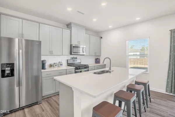 a kitchen with a refrigerator a stove a sink and white cabinets with wooden floor