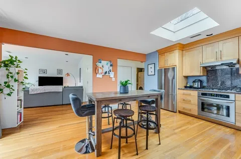 a kitchen with stainless steel appliances kitchen island granite countertop a dining table chairs and a refrigerator