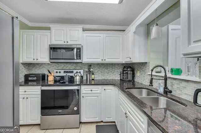 a kitchen with white cabinets a sink stove and microwave