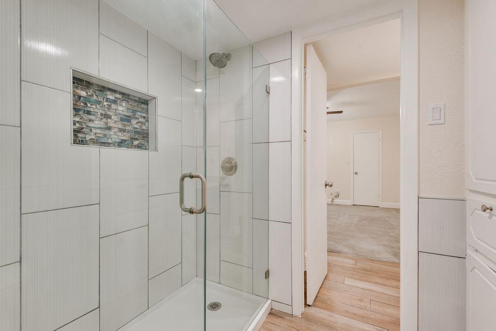 219 West Rochelle Road Irving, TX 75062 - Photo 23 of 29 Glass-enclosed shower with a tiled surround, recessed niche featuring mosaic tile, and a rainfall showerhead
