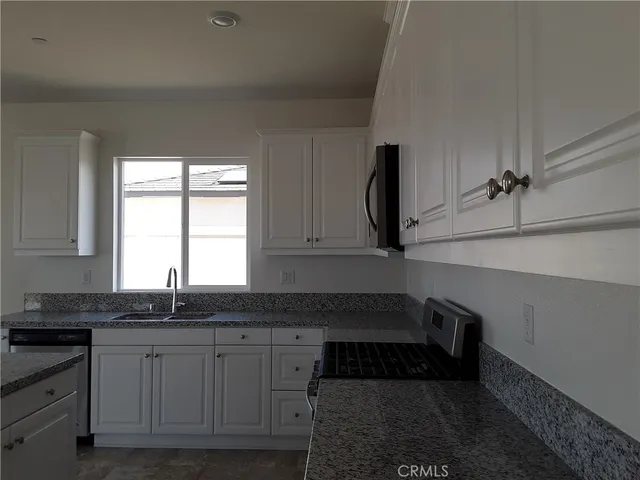 a kitchen with granite countertop a sink and white cabinets