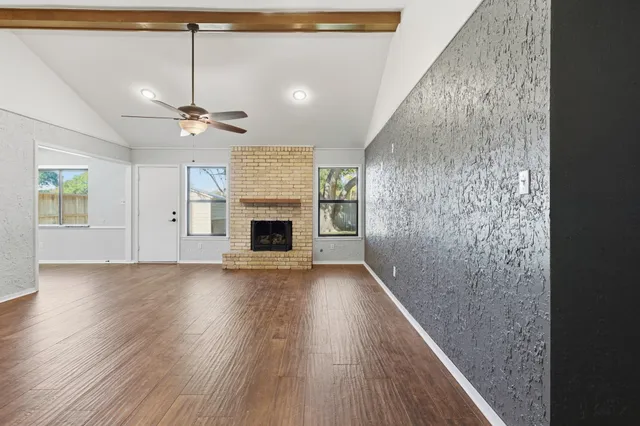an empty room with wooden floor fireplace and ceiling fan