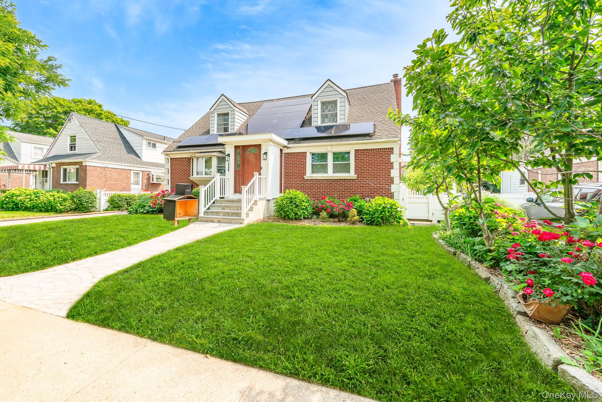 View of front facade featuring brick siding, solar panels, a chimney, and roof with shingles