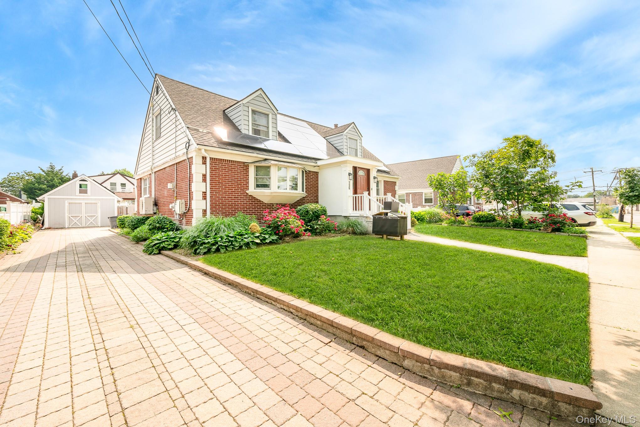 136 Wardwell Road Mineola, NY 11501 - Photo 2 of 25 View of front facade with brick siding, a front yard, roof mounted solar panels, an outbuilding, and a garage
