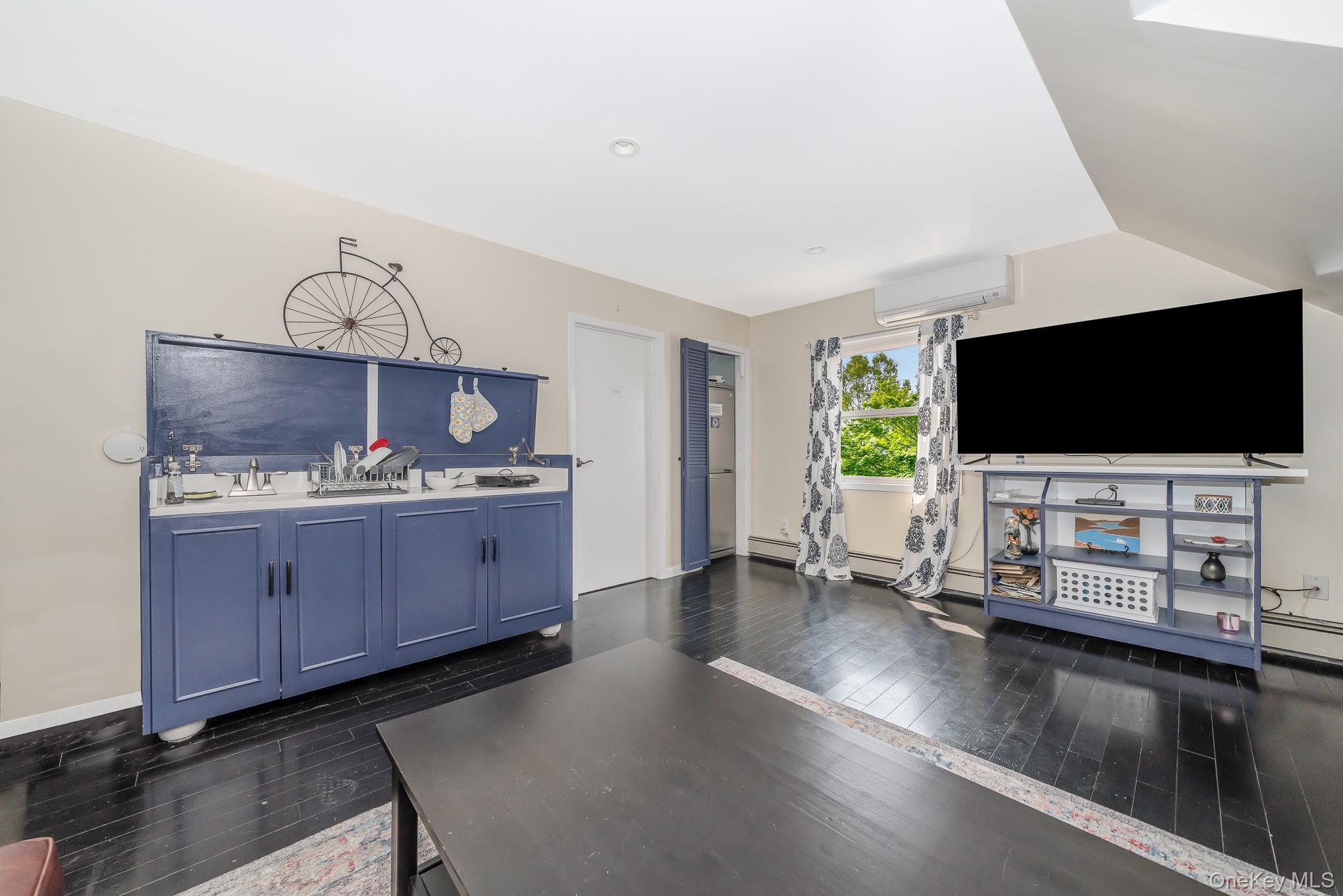 136 Wardwell Road Mineola, NY 11501 - Photo 22 of 25 Unfurnished living room with dark wood finished floors, a wall mounted AC, a baseboard heating unit, baseboards, and vaulted ceiling