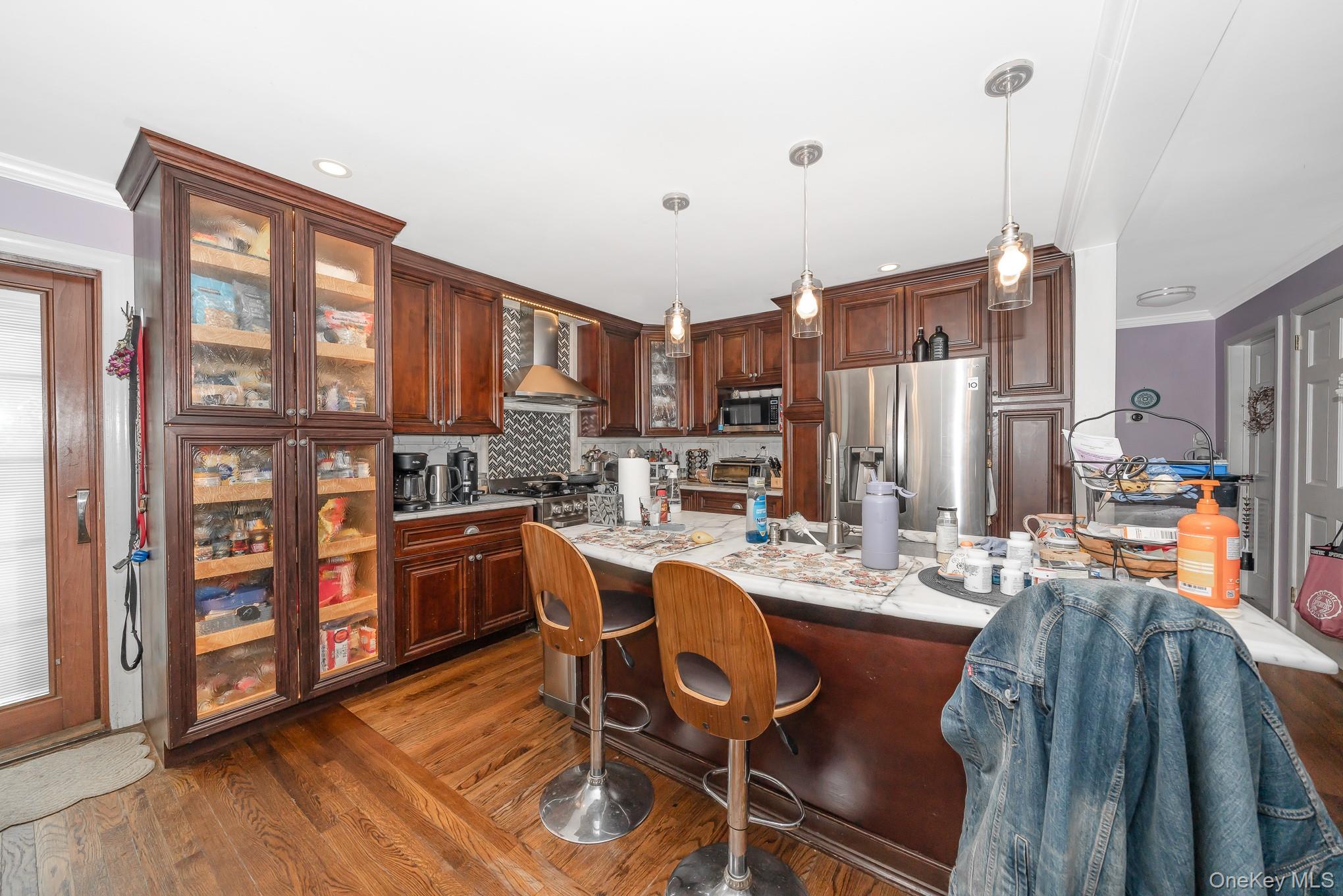 136 Wardwell Road Mineola, NY 11501 - Photo 25 of 25 Kitchen featuring stainless steel appliances, wall chimney range hood, a kitchen breakfast bar, dark wood-type flooring, and backsplash