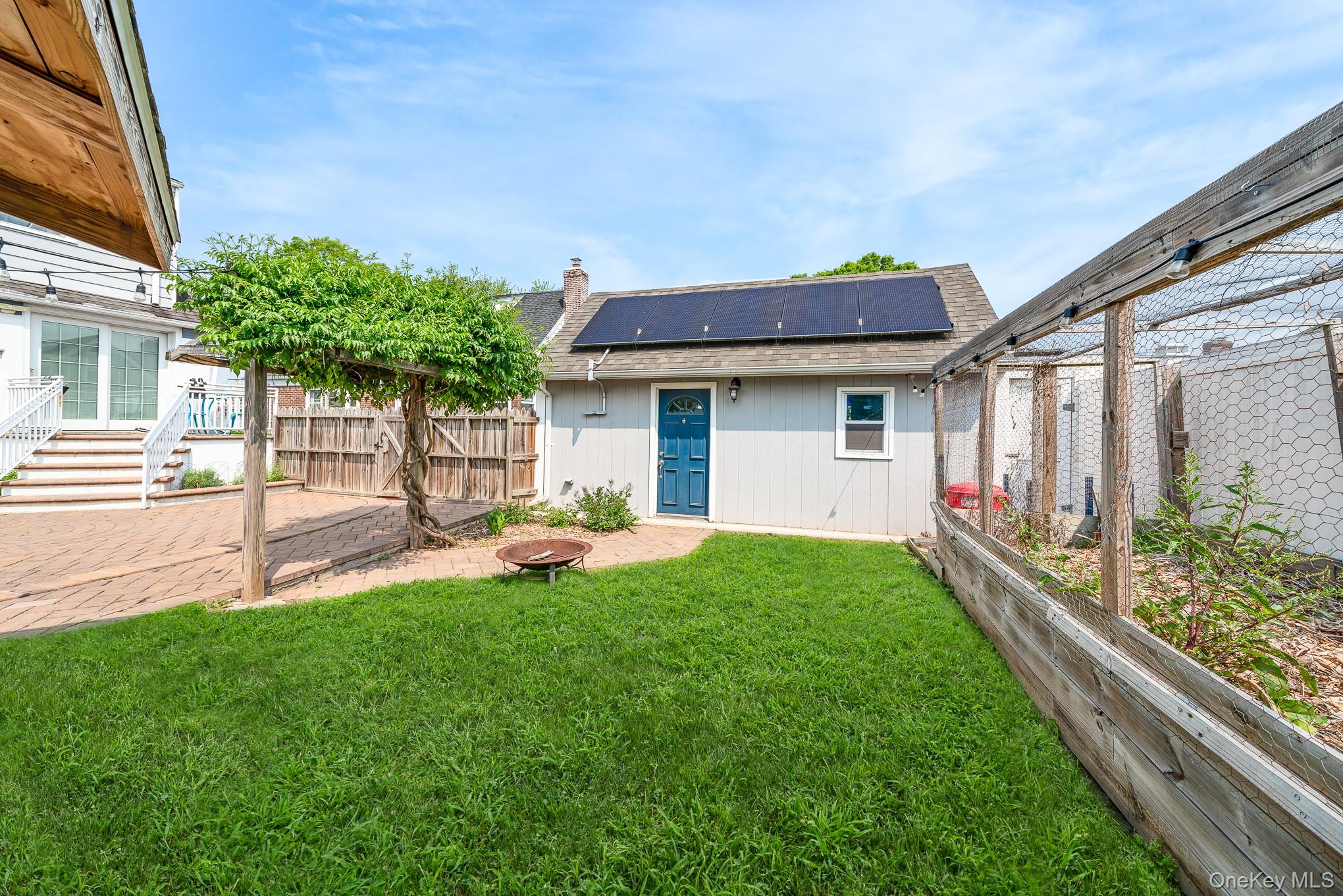 136 Wardwell Road Mineola, NY 11501 - Photo 8 of 25 Rear view of property featuring roof mounted solar panels, roof with shingles, and a chimney