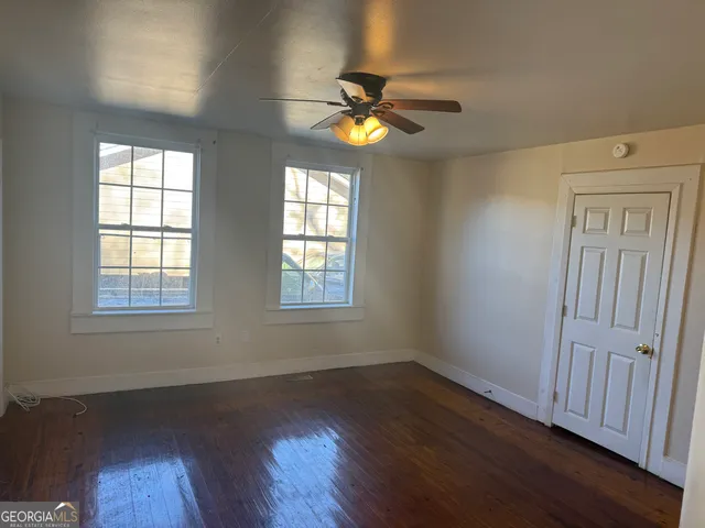 an empty room with wooden floor windows and fan