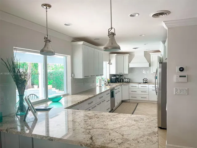 a large kitchen with kitchen island a large window cabinets a sink a stove and a dining table