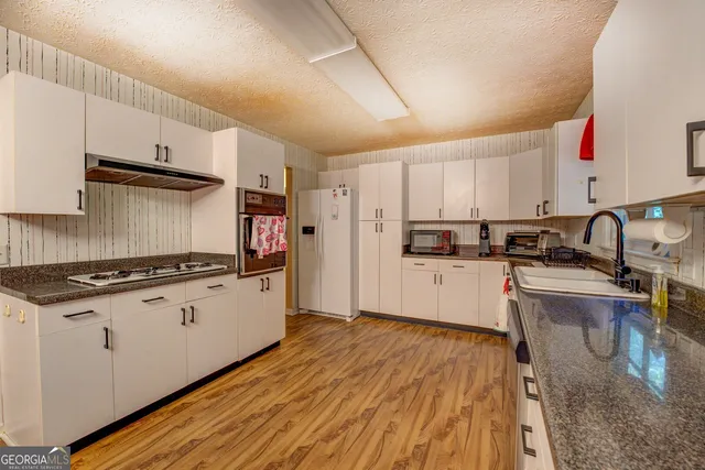 a kitchen with granite countertop a stove top oven a sink dishwasher and a refrigerator with wooden floor