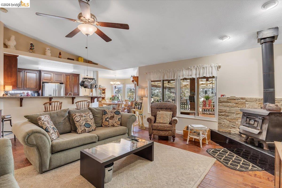 14450 Jacksonville Road Jamestown, CA 95327 - Photo 17 of 85 Vaulted ceiling with an integrated ceiling fan, wood-finish flooring, and a stone-clad fireplace with a wood-burning stove