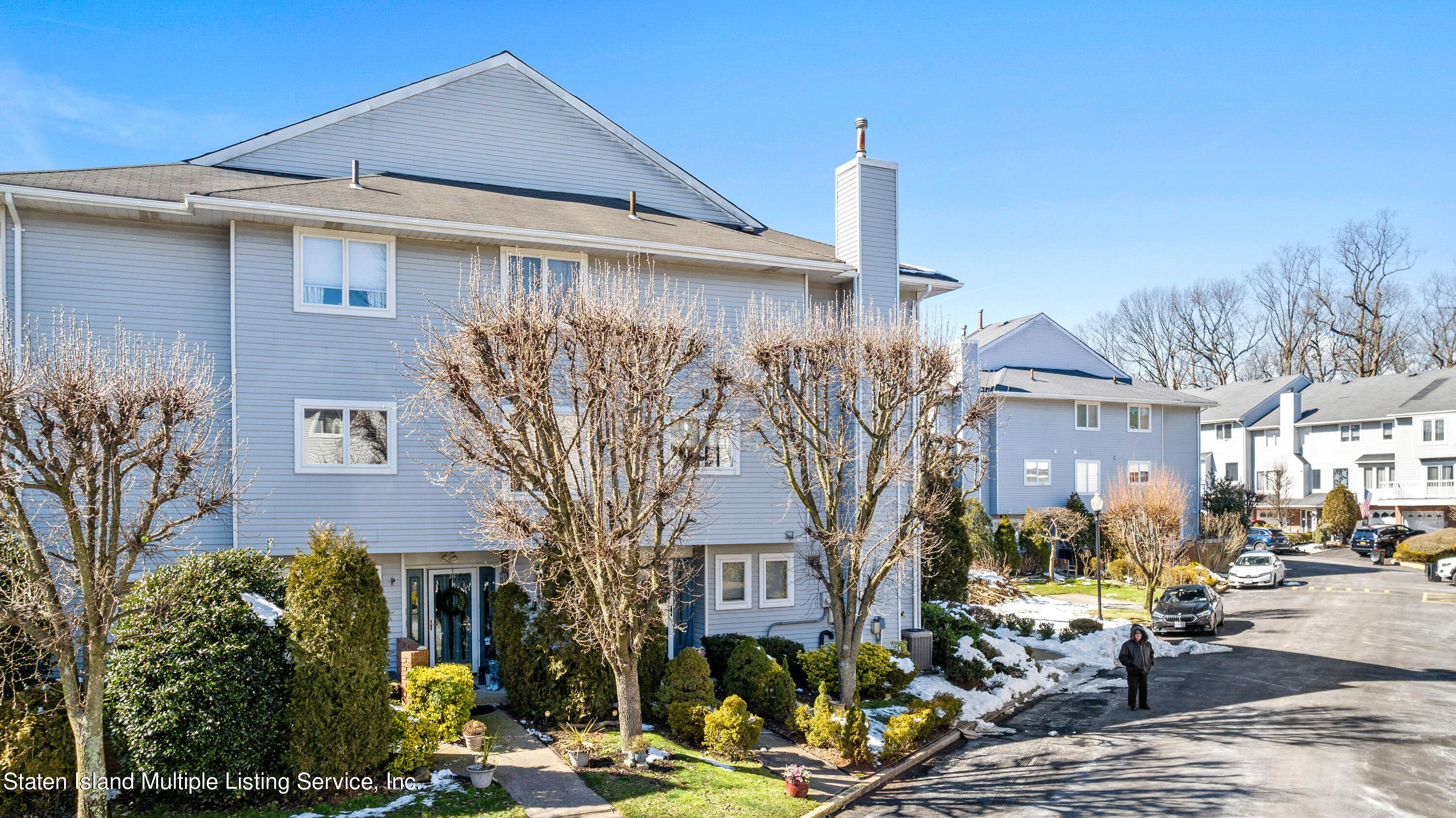 a front view of a building with large trees and plants