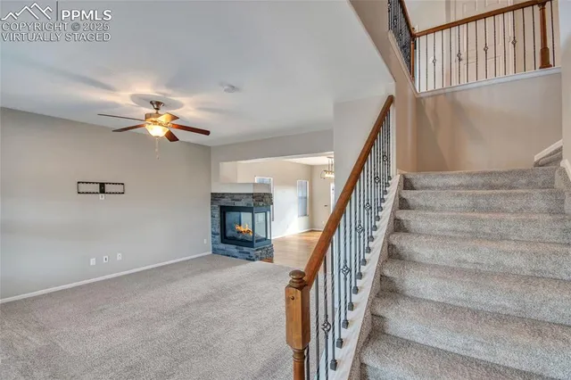 a view of a livingroom with a fireplace a ceiling fan and wooden floor