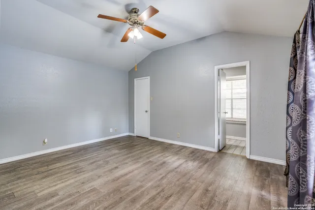 an empty room with wooden floor chandelier fan and windows