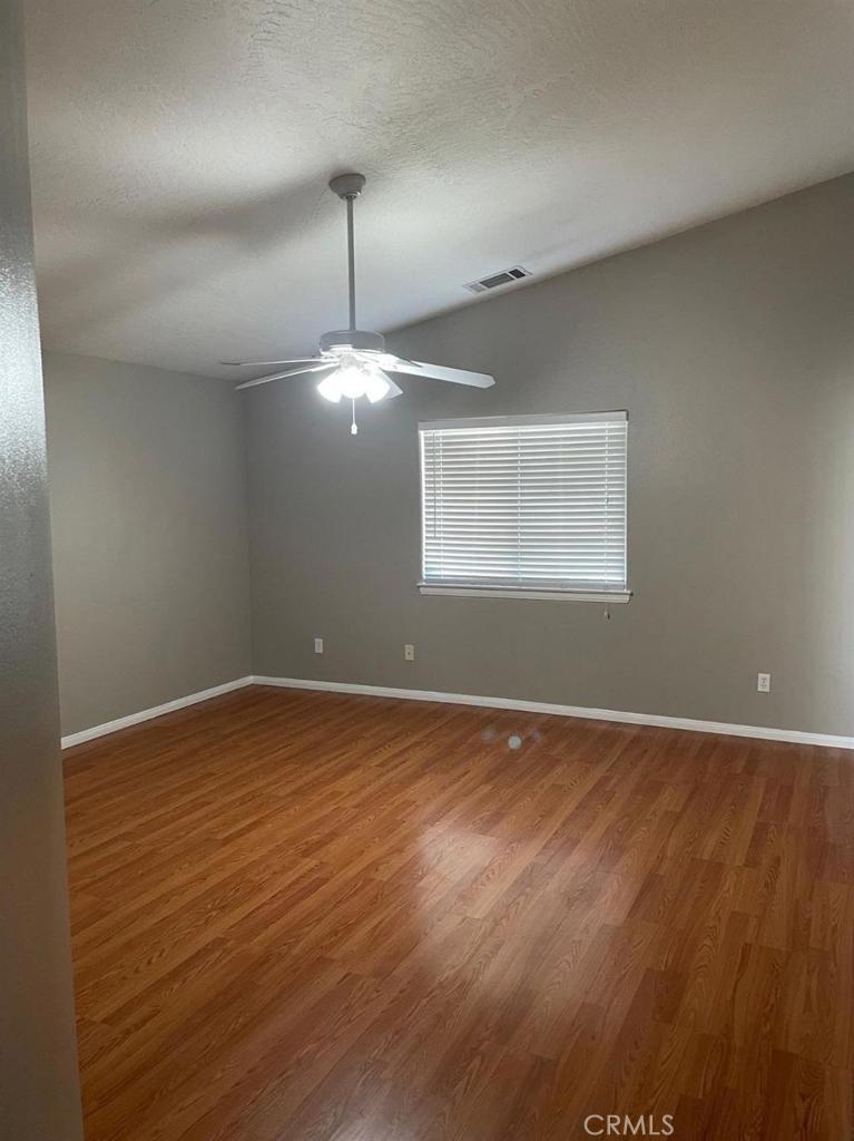 12858 Rain Shadow Road Victorville, CA 92395 - Photo 12 of 15 an empty room with wooden floor chandelier fan and windows