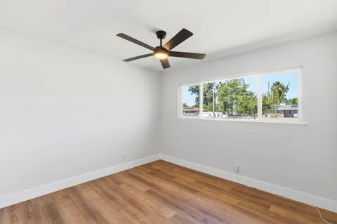 an empty room with wooden floor ceiling fan and windows