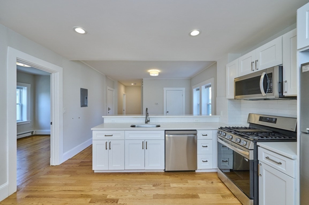67 Wheatland Street, Unit 2 Somerville, MA 02145 - Photo 2 of 19 a kitchen with stainless steel appliances granite countertop a stove top oven a sink dishwasher and white cabinets with wooden floor