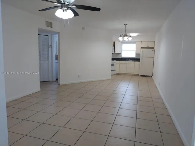 an empty room with kitchen and chandelier fan