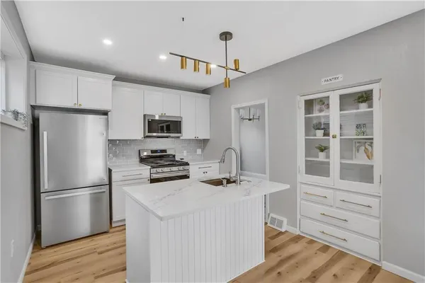 a kitchen that has a refrigerator a stove and white cabinets with wooden floor