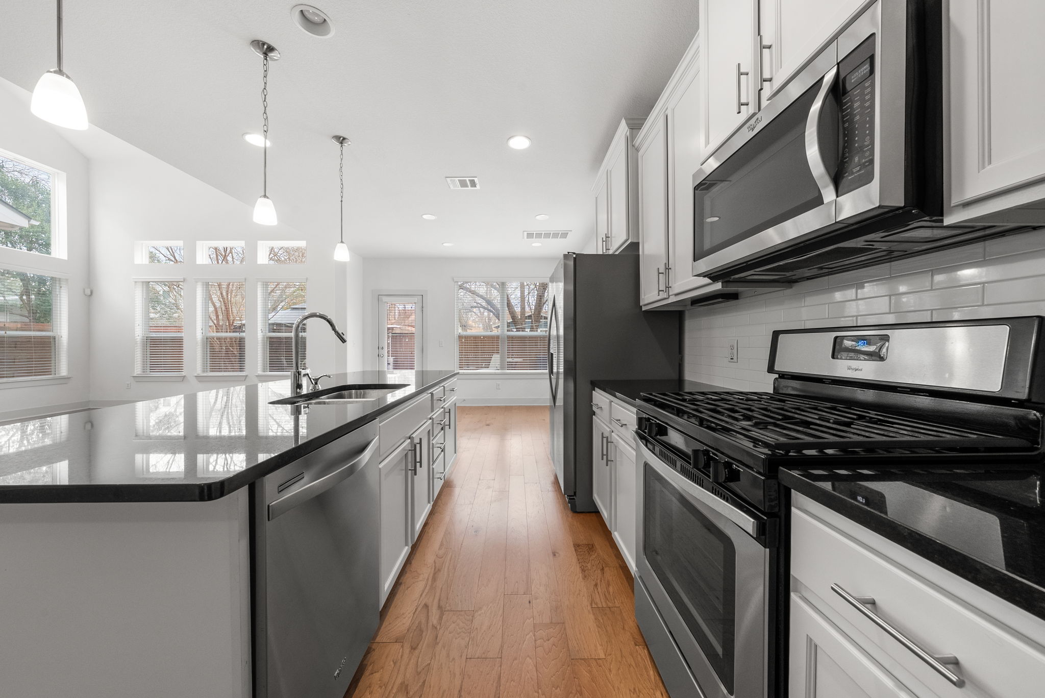 1501 Homespun Road Austin, TX 78745 - Photo 4 of 33 Kitchen featuring stainless steel appliances, dark stone counters, hanging light fixtures, and an island with sink