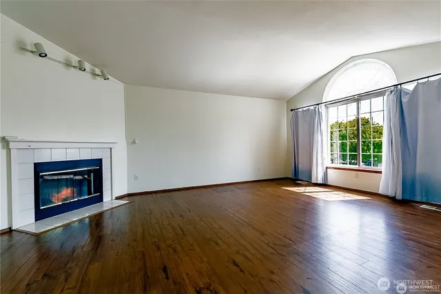 an empty room with wooden floor fireplace and windows