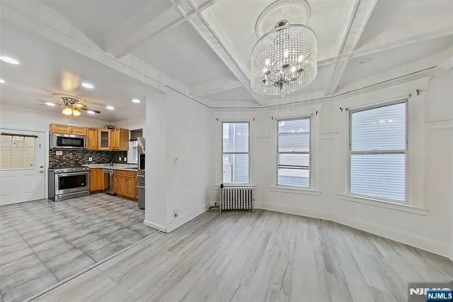 an empty room with wooden floor a kitchen view and windows