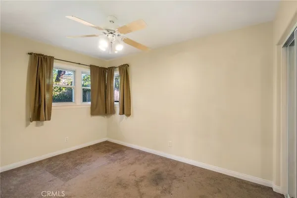 an empty room with chandelier fan and windows