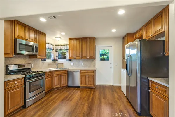 a kitchen with stainless steel appliances granite countertop wooden cabinets a refrigerator a stove a sink and dishwasher with wooden floor