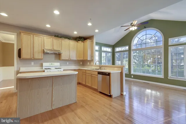 a kitchen with stainless steel appliances granite countertop a stove a sink a refrigerator and white cabinets with wooden floor