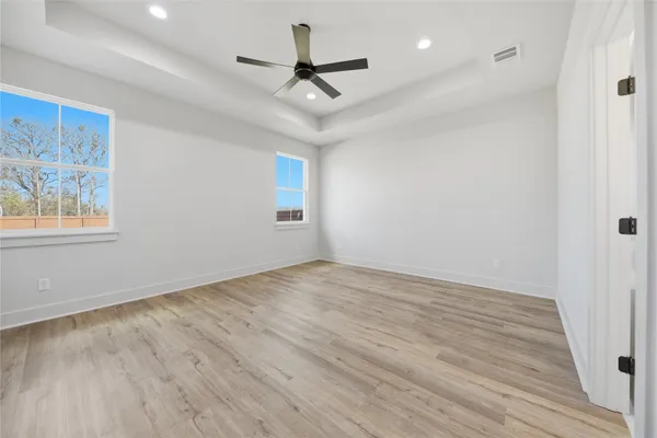 an empty room with wooden floor ceiling fan and windows