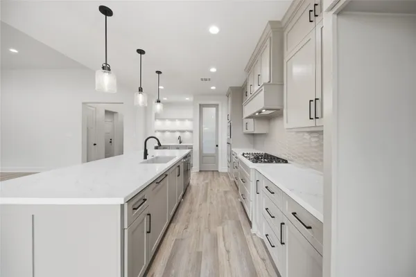 a large kitchen with kitchen island a stove a sink a refrigerator and white cabinets with wooden floor