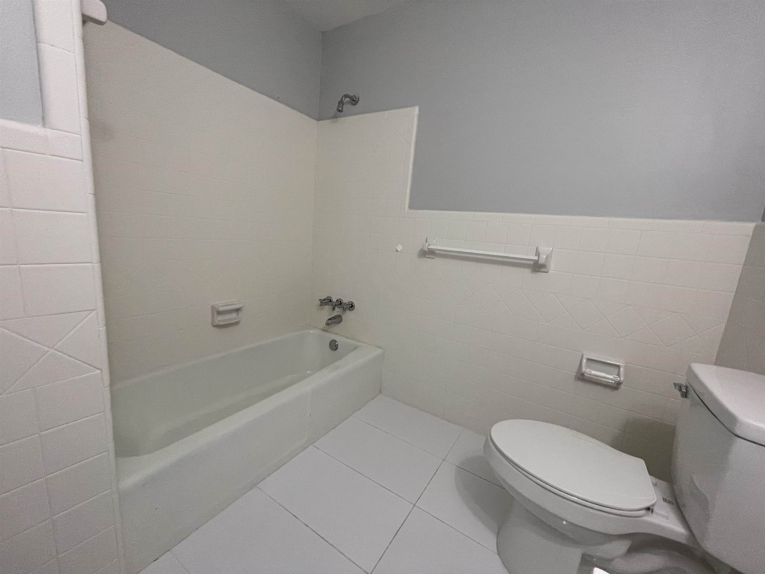 379 McElroy Road Memphis, TN 38120 - Photo 12 of 22 White tiled bathroom featuring a full bathtub with chrome fixtures, a white toilet, and tile flooring