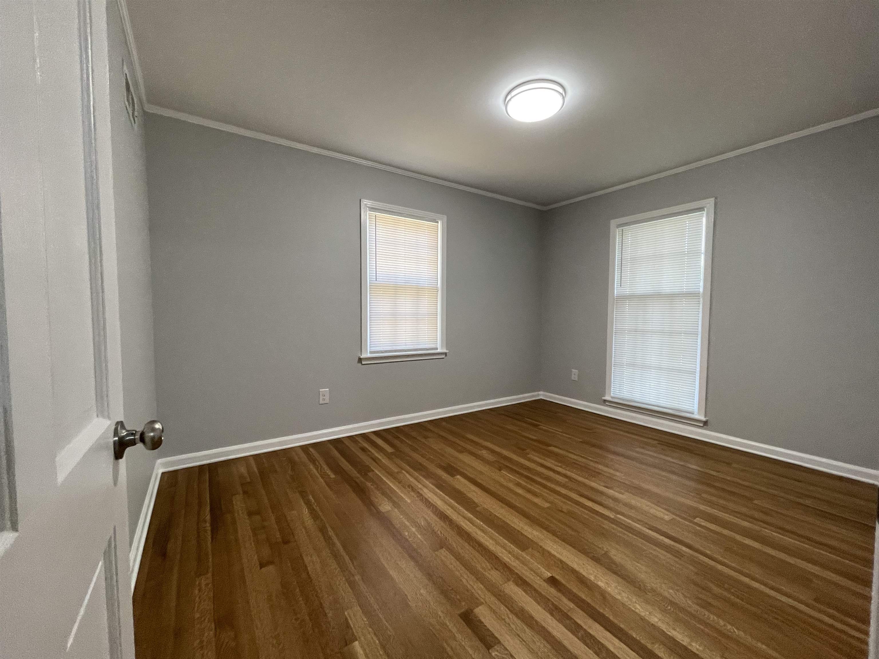 379 McElroy Road Memphis, TN 38120 - Photo 14 of 22 Spacious room featuring wood-finish flooring, two windows with blinds, a ceiling-mounted light fixture, crown molding, and painted walls