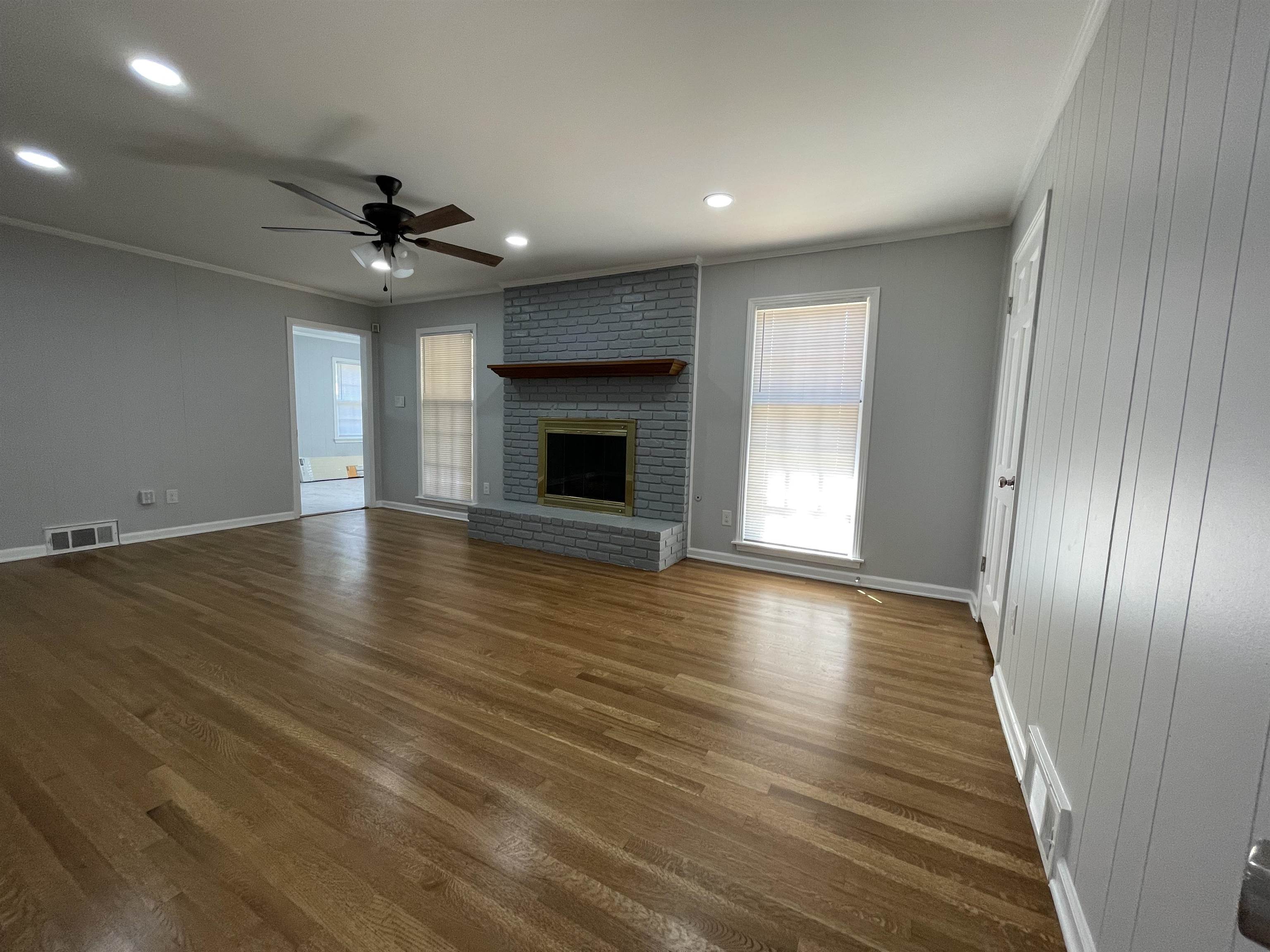 379 McElroy Road Memphis, TN 38120 - Photo 4 of 22 Expansive living area featuring wood-finish flooring, a painted brick fireplace with a wood mantle, a ceiling fan with integrated lighting, recessed lighting, and vertical plank wall paneling