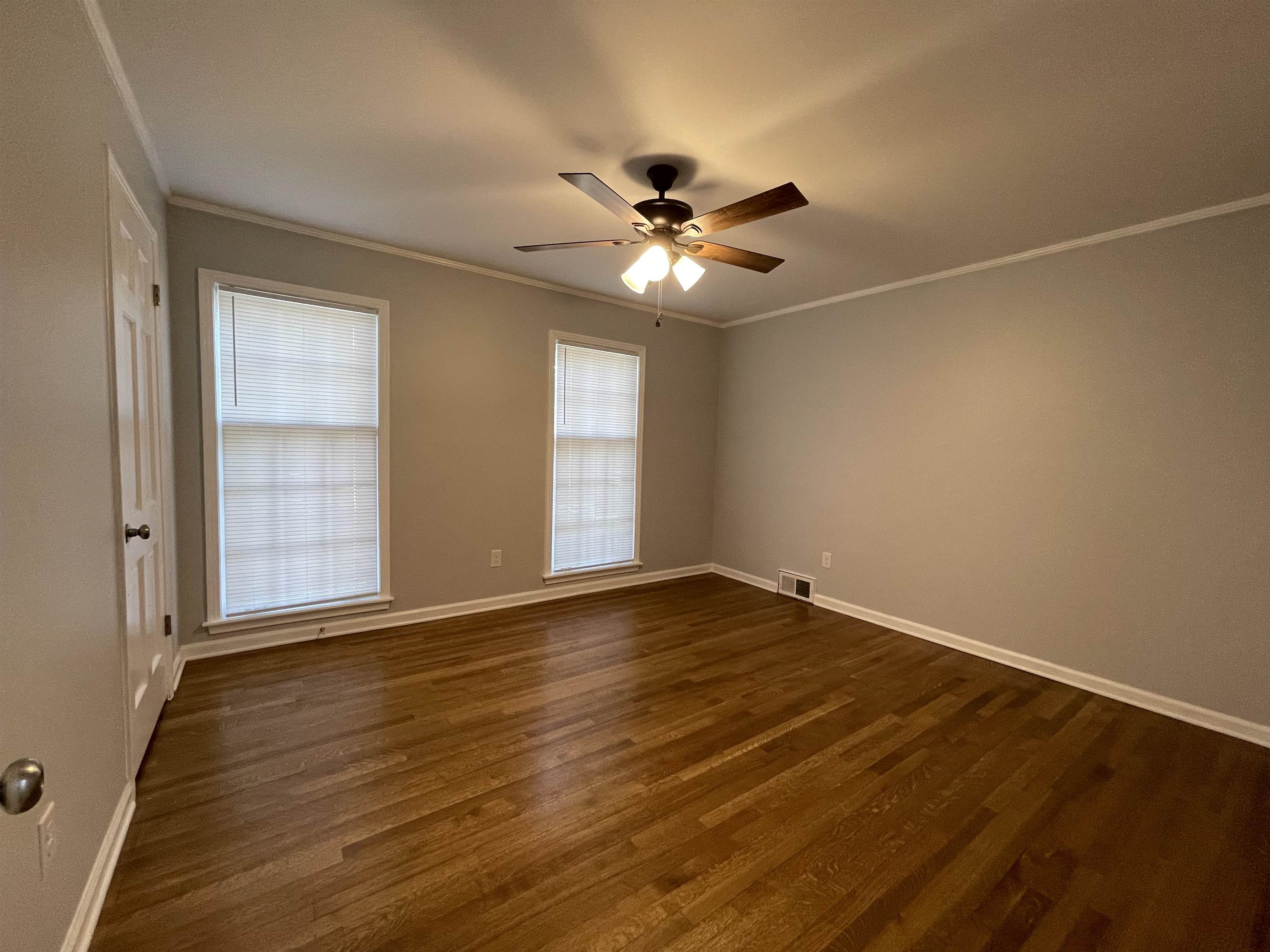 379 McElroy Road Memphis, TN 38120 - Photo 10 of 22 Spacious room featuring wood-finish flooring, two large windows with blinds, a ceiling fan with integrated lighting, a white painted door, and white baseboards and crown molding