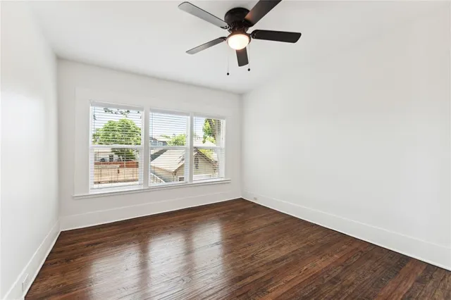 an empty room with wooden floor chandelier fan and windows