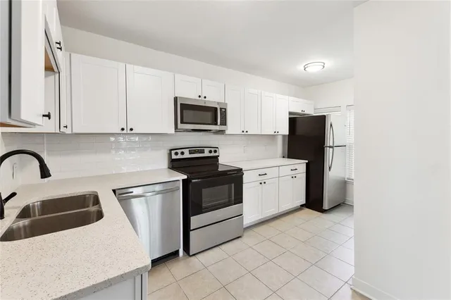a kitchen with stainless steel appliances white cabinets a sink a stove a microwave and a refrigerator
