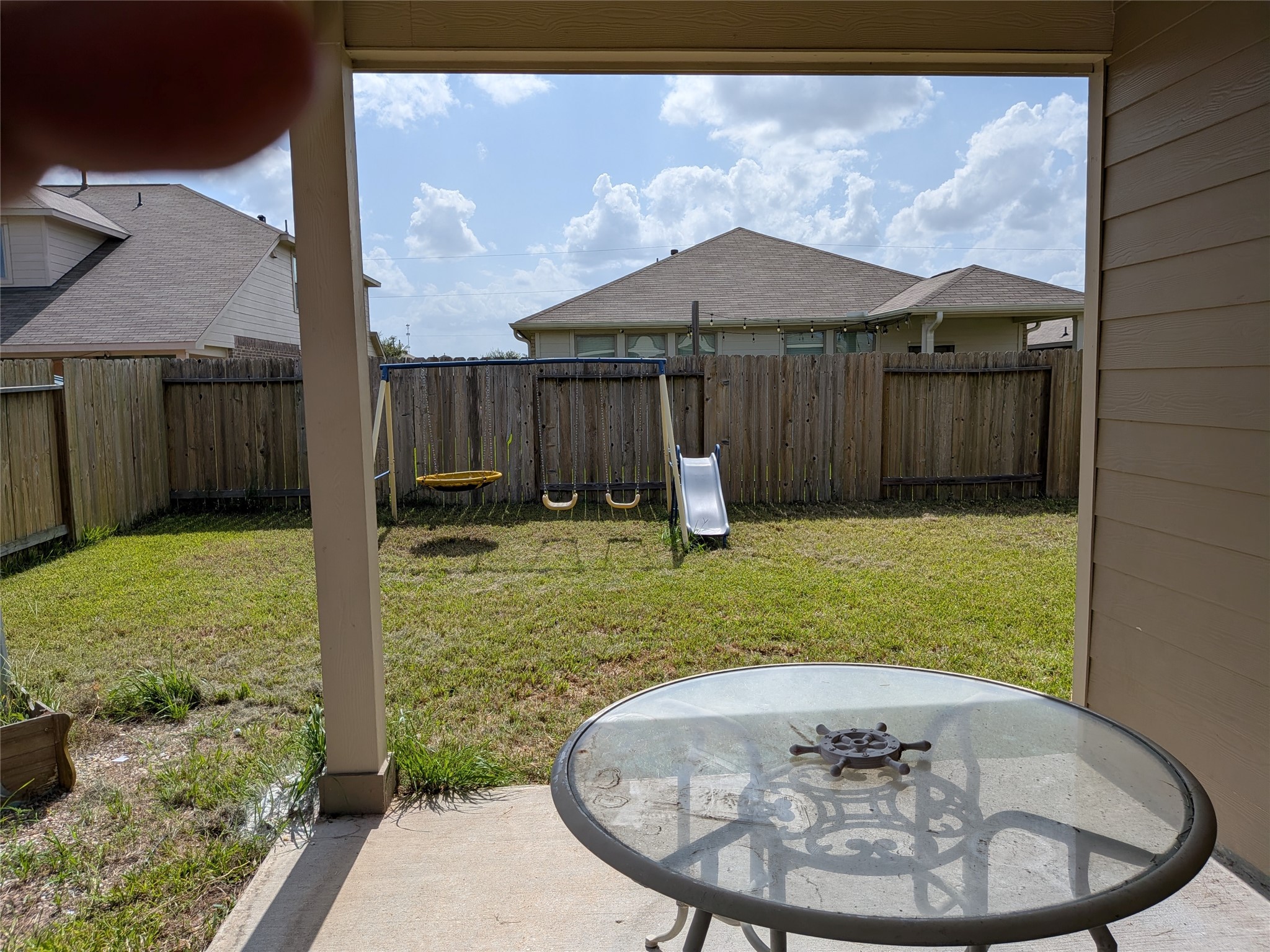 15730 Joe Dimaggio Street Splendora, TX 77372 - Photo 19 of 20 This backyard features a covered patio with a glass table, overlooking a grassy area with a wooden fence for privacy. The space includes a swing set and slide, perfect for families.