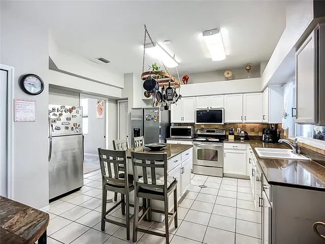 a kitchen with stainless steel appliances kitchen island granite countertop a refrigerator a stove top oven a sink dishwasher and a dining table with wooden floor