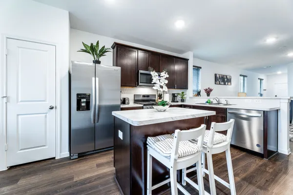 a kitchen with granite countertop a refrigerator a stove a sink and a dining table with wooden floor