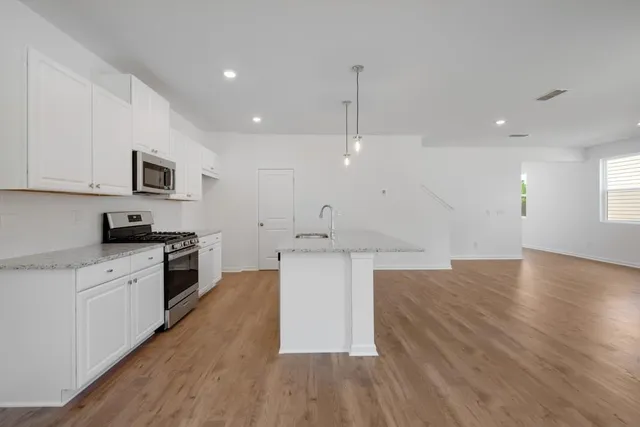 a large kitchen with stainless steel appliances granite countertop a large center island a sink dishwasher a refrigerator and white cabinets with wooden floor