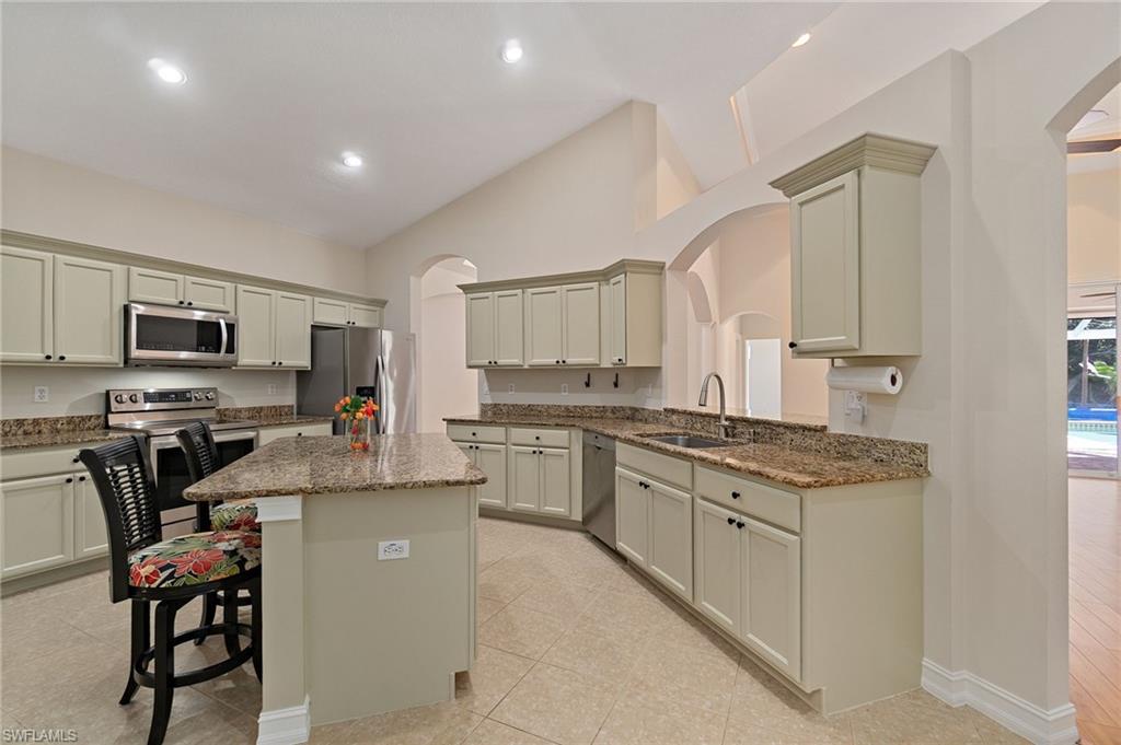 1158 Oakes Boulevard Naples, FL 34119 - Photo 14 of 40 Kitchen featuring arched walkways, natural stone counters, a breakfast bar area, stainless steel appliances, and a kitchen island