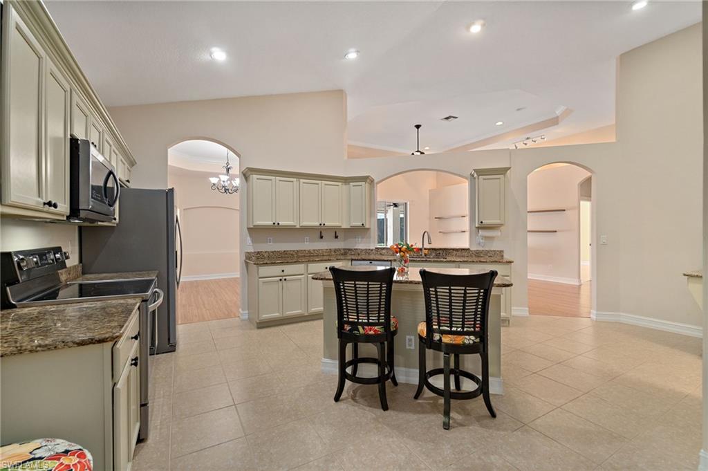 1158 Oakes Boulevard Naples, FL 34119 - Photo 15 of 40 Kitchen with arched walkways, range with electric stovetop, natural stone counters, a breakfast bar, and vaulted ceiling
