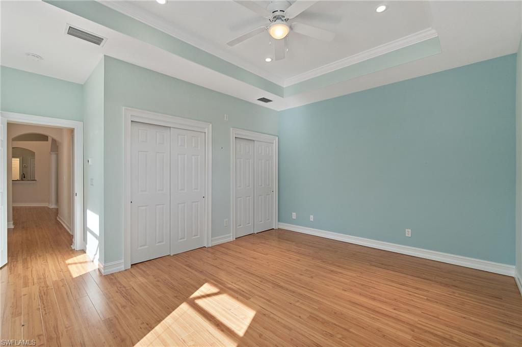 1158 Oakes Boulevard Naples, FL 34119 - Photo 31 of 40 Unfurnished bedroom featuring multiple closets, arched walkways, light wood-style floors, ceiling fan, and a tray ceiling