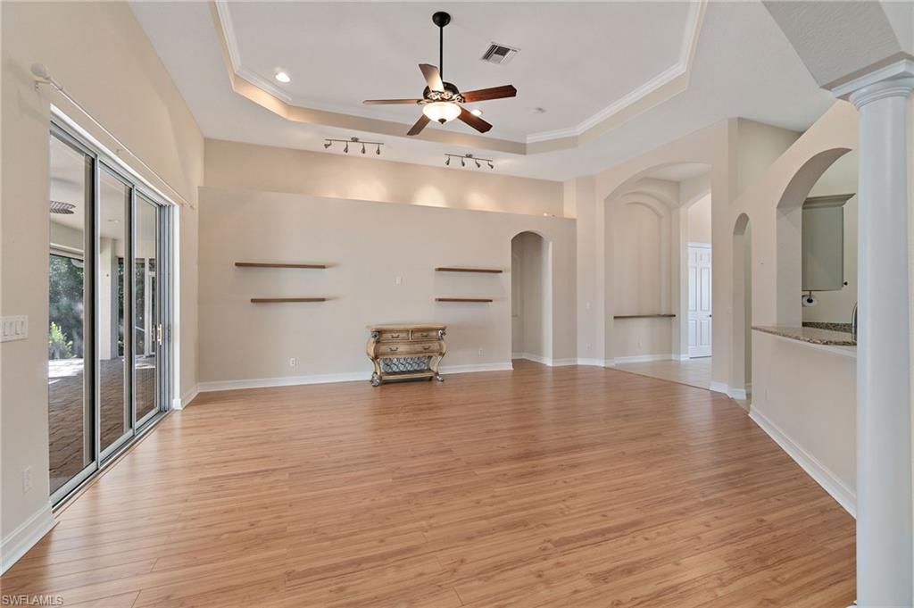 1158 Oakes Boulevard Naples, FL 34119 - Photo 8 of 40 Unfurnished living room featuring light wood-style flooring, ornamental molding, ceiling fan, a tray ceiling, and arched walkways